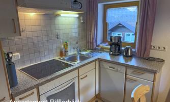A modern kitchen with light walls and a large window front. It is well-equipped with appliances and offers a cozy atmosphere.