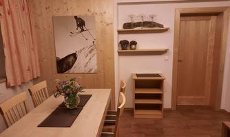 A cozy room with a wooden table and chairs. A picture of a skier hangs on the wall, and a shelf is adorned with decorations.