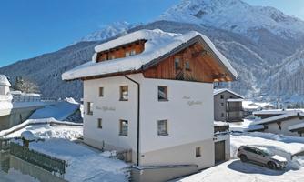A snow-white house with a wooden floor, surrounded by snow-covered mountains. The landscape depicts a winter idyll.