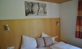 A cozy bedroom with a wooden headboard and two pillows. On the wall hangs an artwork featuring winter trees.