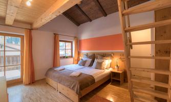 A cozy bedroom with a large bed and warm wooden furniture. Large windows provide plenty of light and a view outside.