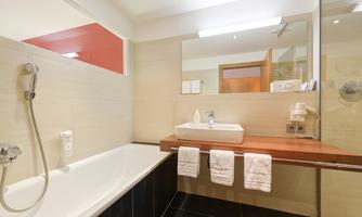 A modern bathroom with a bathtub and a sink on a wooden shelf. The walls are in neutral colors and there are large mirrors.