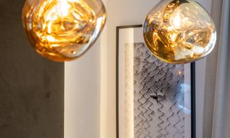 Two stylish, golden lamps hang above a modern artwork on the wall. The picture emanates an elegant and cozy atmosphere.