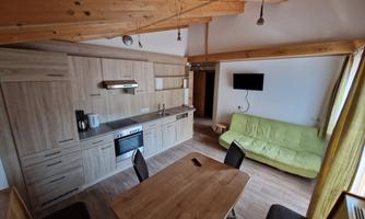A modern kitchen unit made of wood with a dining area and a green sofa. The room is bright and friendly, perfect for a cozy stay.