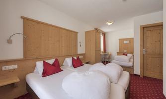 A cozy hotel room with two beds and wooden paneling. Red cushions and a simple table complete the inviting atmosphere.