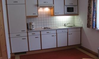 A modern kitchen unit with white cabinets and a stove. The kitchen unit is bright and well-organized, with a microwave and a kettle.