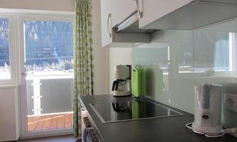 A modern kitchen with a cooktop, a coffee machine, and a white kettle. Through the window, there is a beautiful view of the landscape.