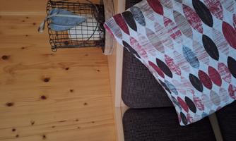 A cozy sofa with a colorful pillow and a decorative basket on a shelf. The basket contains a candle and has a leaf as decoration.