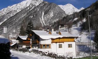 A snowy landscape with mountains and a tranquil village. The houses are covered in snow and offer a picturesque winter view.