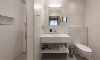 A modern bathroom with white tiles and a minimalist design. It includes a shower, a sink, and a toilet.