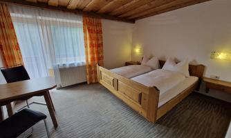 A cozy bedroom with a wooden double bed and two nightstands. The windows are dressed with curtains and the room has a warm, inviting ambiance.