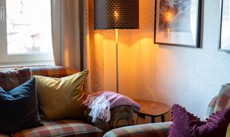 A cozy living room with a checked sofa and colorful cushions. A floor lamp provides warm light and a relaxed atmosphere.