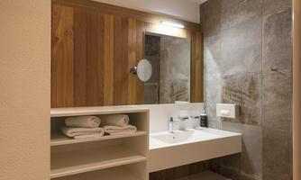 A modern bathroom with wood details and an elegant sink. Towels are neatly placed on a shelf.