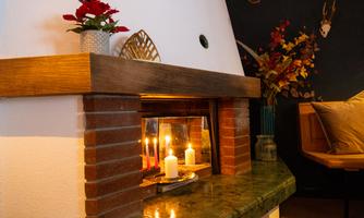 A cozy fireplace with burning candles and decorative flower arrangements. The atmosphere is warm and inviting.