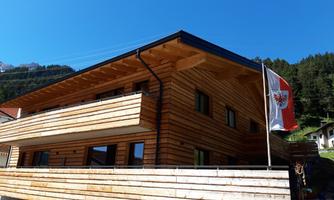 A modern wooden house with a balcony and clear blue sky. A flag is waving on the façade.