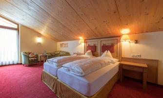 A cozy hotel room with two beds and wooden ceilings. There is a small table and a seating area with a sofa.