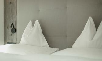A cozy bedroom with two beds and white pillows. The wall has a soft texture and brings a relaxed atmosphere.