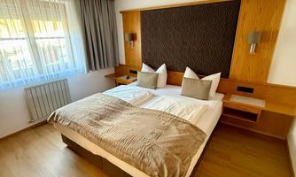 A cozy bedroom with a large bed and modern furnishings. The windows let in plenty of daylight and the room has a warm atmosphere.