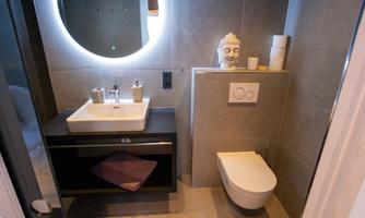 A modern bathroom with an elegant sink and a round mirror. The decor is simple and stylish, with a Buddha head as decoration.