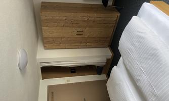 A simple room with two single beds and a wooden wardrobe. There is a chair and a view of the entrance.