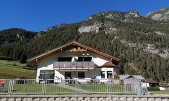 A modern building amidst green meadows and high mountains. The clear sky contributes to the picturesque atmosphere.