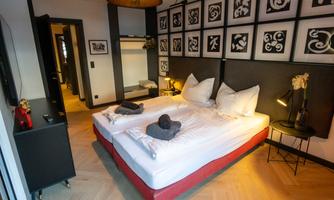 A modern bedroom with a double bed and decorative pictures on the wall. The room has a warm wooden floor and a cozy atmosphere.