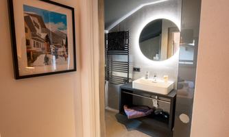 A modern bathroom with a round mirror and an elegant sink unit. A framed picture hangs on the wall and there are towels on the floor.