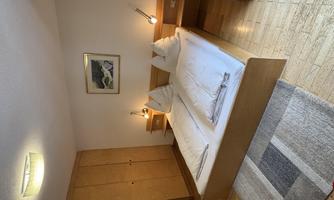 A simple and modern bedroom with a double bed and two pillows. The room features a wardrobe and soft lighting.