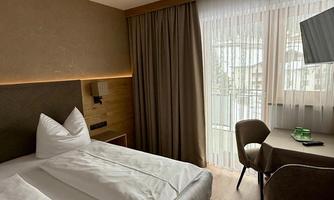 An elegant room with a double bed and a table. Large windows let in plenty of light and offer a view of the surroundings.