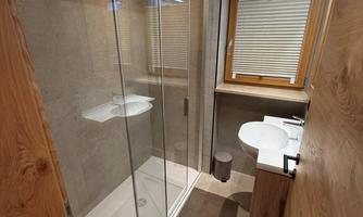 A modern bathroom with a glass shower and a contemporary sink. The space is bright and designed with wooden details.