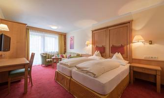 A cozy hotel room with two single beds and a small table. The room is bright and cheerful, with large windows and modern furnishings.