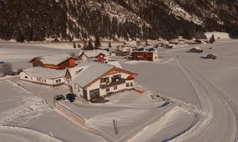 A snowy landscape with several houses. The surroundings are quiet and surrounded by mountains.