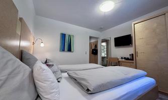 A modern room with a double bed and pillows. Art pieces hang on the wall, and there is a television as well as a table in the background.