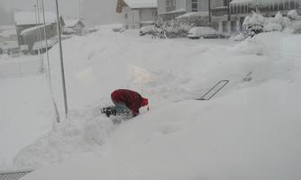 A child is playing in the deep snow and digging in the white winter wonderland. In the background, snow-covered houses and a snowy landscape can be seen.