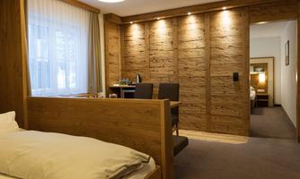 A modern hotel room with wood paneling and comfortable furniture. There is a desk and a separate area for relaxing.