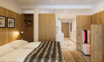 A modern room with wood paneling and a large double bed. The decor is bright and inviting, with a small kitchen in the corner.
