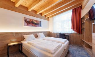 A modern room with a wooden ceiling and two single beds. Bright colors and large windows create a cozy atmosphere.