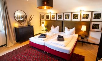 A cozy bedroom with two beds and stylish furniture. The walls are decorated with artworks, and the lighting creates a pleasant atmosphere.