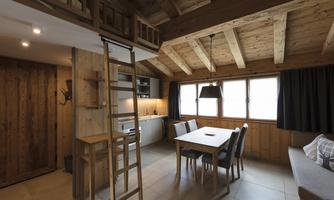 A cozy wooden apartment with an open kitchen and dining table. Large windows provide plenty of light and a warm, inviting space.
