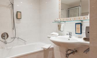 A modern bathroom with a bathtub and a sink. The walls are brightly tiled, and there is a shower cubicle as well as towels.