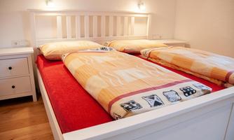 A cozy bedroom with a double bed and two blankets. The walls are light, and there is a nightstand next to the bed.
