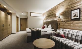 A modern hotel room with wooden paneling and a cozy bed. There is a seating area with a round table and a large window.