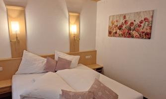 A cozy bedroom with a large bed and decorative pillows. A picture of blooming flowers hangs on the wall.