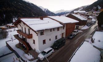 A charming snow-covered building in a mountainous landscape. Cars are parked along the road, surrounded by snow-covered mountains.
