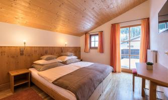 A bright and cozy bedroom with a double bed and wooden walls. Large windows provide a view outside and ensure plenty of daylight.
