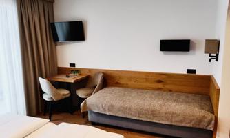 A cozy hotel room with two beds, a table, and a television. The decor is modern and welcoming with wood panels and soft colors.