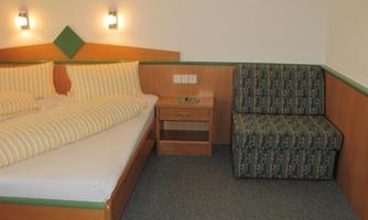 A cozy hotel room with a double bed and a green couch. The walls are light, and the lighting creates an inviting atmosphere.