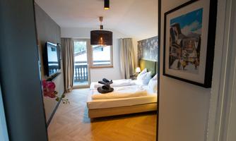 A cozy bedroom with two beds and modern furniture. Large windows let in plenty of daylight, creating an inviting atmosphere.