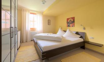 A cozy bedroom with a large bed and beige walls. The room has large windows that let in plenty of natural light.