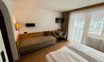 A cozy hotel room with two single beds and an additional sofa bed. Large windows provide plenty of daylight.